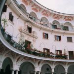 Pátio histórico em Sevilha, com arcadas ornamentadas, colunas e balcões ao redor de um espaço circular.