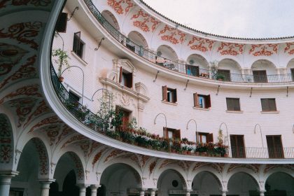 Pátio histórico em Sevilha, com arcadas ornamentadas, colunas e balcões ao redor de um espaço circular.