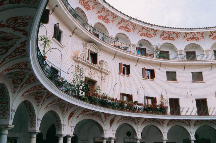 Pátio histórico em Sevilha, com arcadas ornamentadas, colunas e balcões ao redor de um espaço circular.