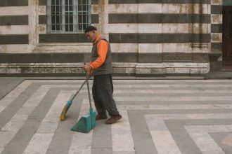 Pessoa varrendo o pátio de um edifício urbano.