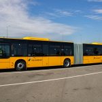 Ônibus urbano articulado amarelo estacionado em uma área aberta durante o dia.