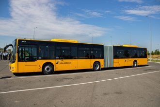 Ônibus urbano articulado amarelo estacionado em uma área aberta durante o dia.