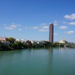 Vista panorâmica de Sevilha com a Torre Sevilla e o rio Guadalquivir sob céu azul.