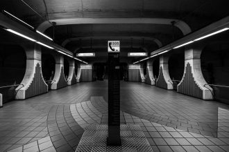 Estação de metrô moderna, em preto e branco, com um posto de telefone de emergência em destaque.