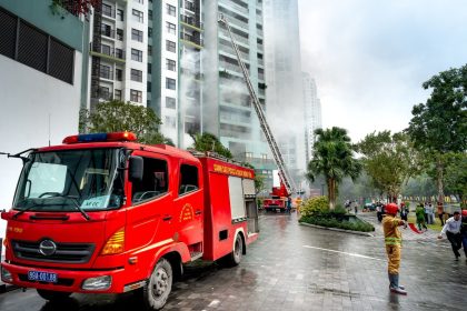 Bombeiros combatem a fumaça de um incêndio em um edifício residencial, com caminhões de emergência na rua.