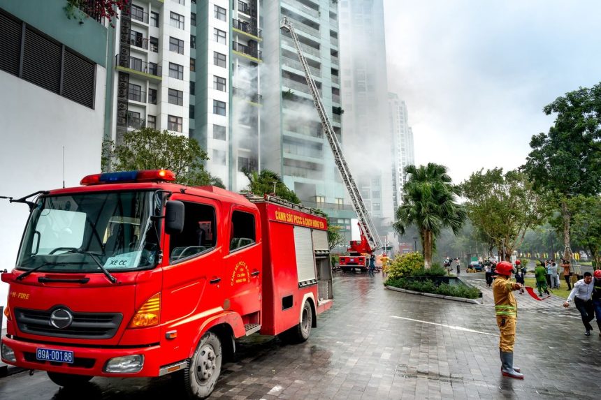 Bombeiros combatem a fumaça de um incêndio em um edifício residencial, com caminhões de emergência na rua.