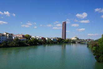 Vista panorâmica de Sevilha com a Torre Sevilla e o rio Guadalquivir sob céu azul.