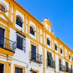 Fachada amarela e branca de um edifício histórico de Sevilha, com varandas e elementos arquitetônicos tradicionais.