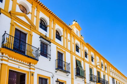 Fachada amarela e branca de um edifício histórico de Sevilha, com varandas e elementos arquitetônicos tradicionais.