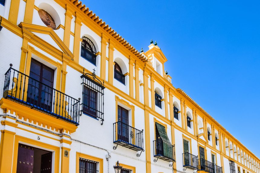 Fachada amarela e branca de um edifício histórico de Sevilha, com varandas e elementos arquitetônicos tradicionais.