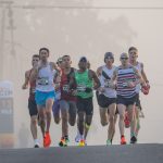 Corredores participam de uma prova de atletismo em ruas urbanas durante uma manhã enevoada.
