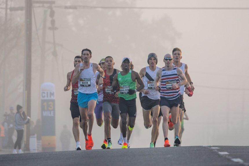 Corredores participam de uma prova de atletismo em ruas urbanas durante uma manhã enevoada.